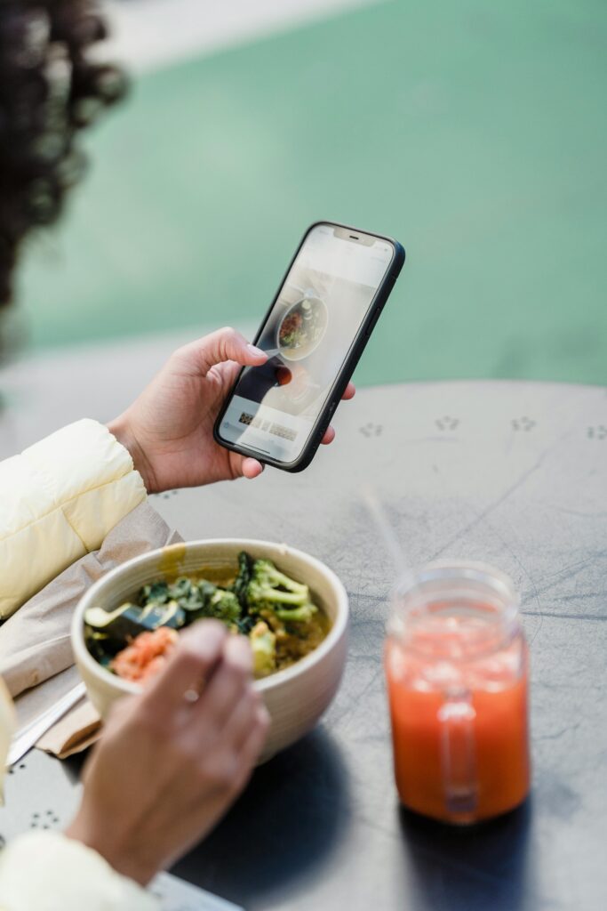 Crop blogger with smartphone and tasty vegetarian salad in cafeteria